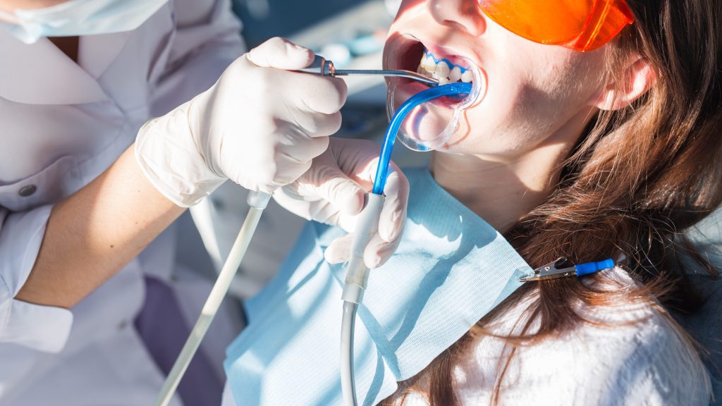 Close-up portrait of a female patient at dentist in the clinic. Teeth whitening procedure with ultraviolet light UV lamp.